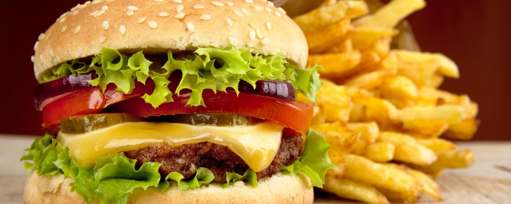 Big cheeseburger with french fries in bag paper on wooden table on red dpotlight background