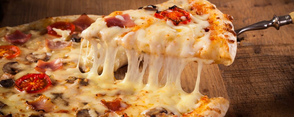 Hot pizza slice with melting cheese on a rustic wooden table.