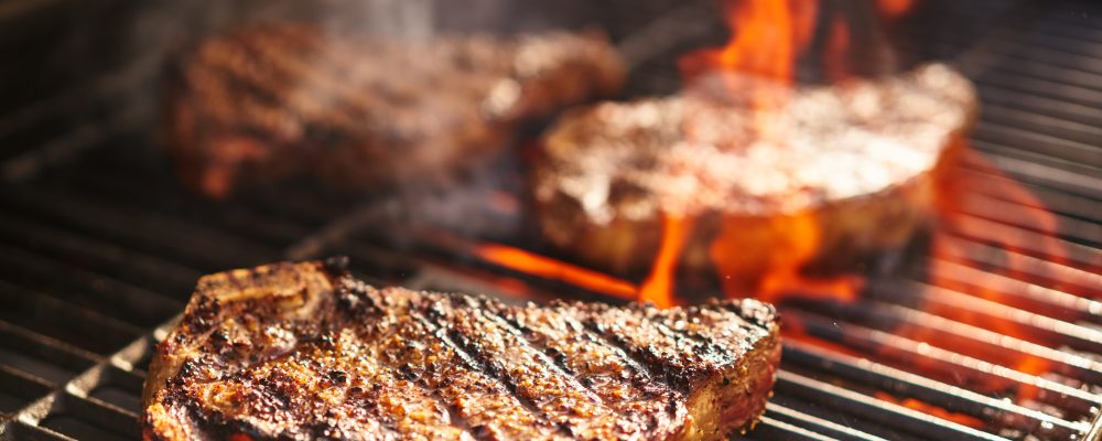 steaks cooking over flaming grill