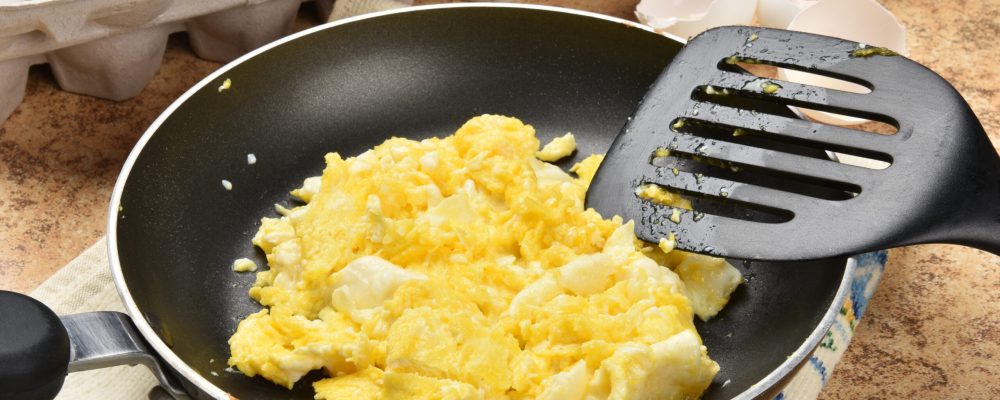 Scrambled eggs in a frying pan near the egg carton
