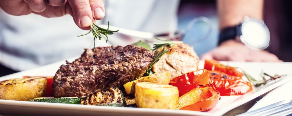 Chef in hotel or restaurant kitchen cooking only hands. Prepared beef steak with vegetable decoration.