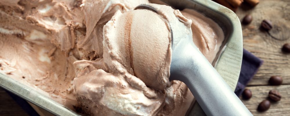 Homemade ice cream with scoop in frozen metallic container on wooden background