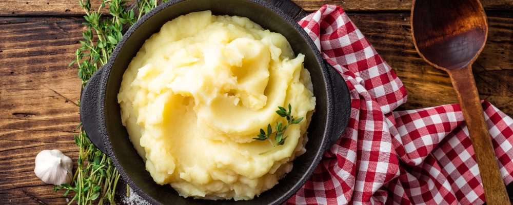 Mashed potatoes, boiled puree in cast iron pot on dark wooden rustic background, top view