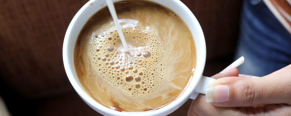 pouring creamer into a cup of hot coffee