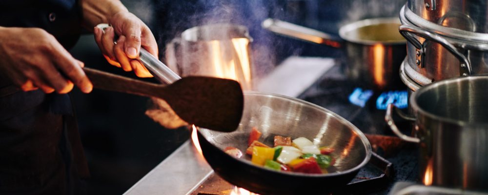 Hands of cook frying vegetables on pan