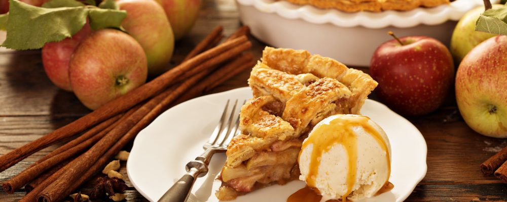 Piece of an apple pie with ice cream scoop and caramel sauce on a plate, fall baking concept