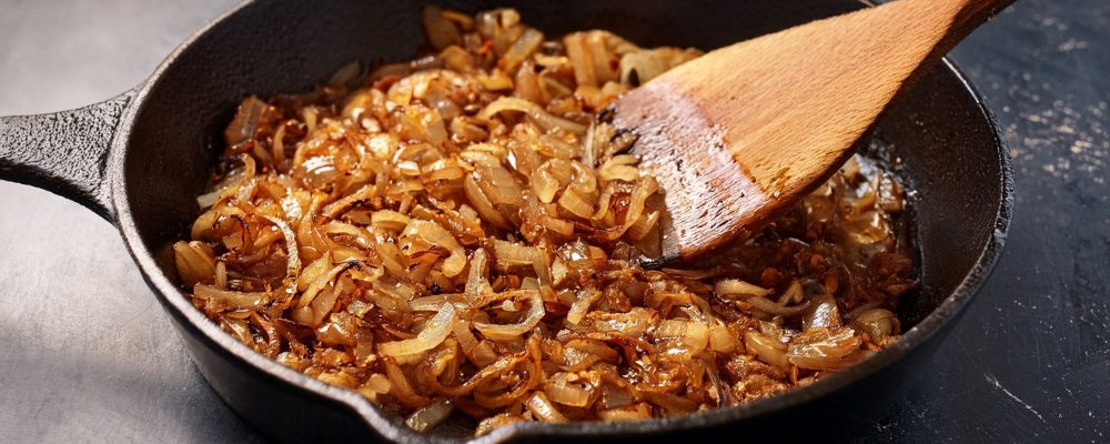 golden caramelized onions are sauteed in a cast iron skillet stirred with a wooden spatula