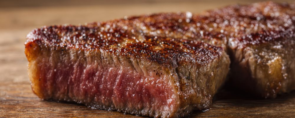 Juicy ribeye steak with visible grill marks, resting on a rustic wooden surface. menu design, packaging mockups, designed for food delivery and cloud-kitchen brand materials.