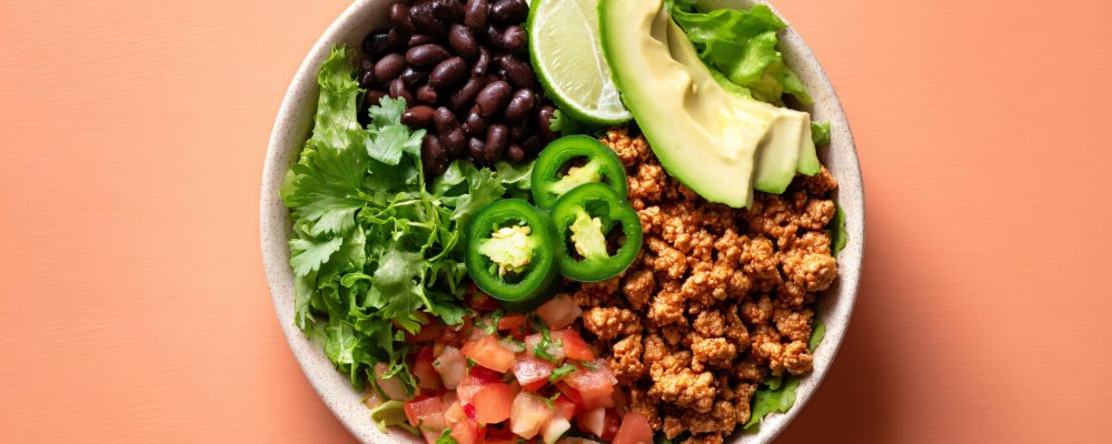 Ground turkey taco bowl prep on pastel peach backdrop