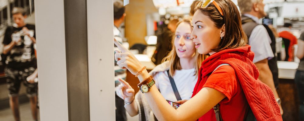A woman orders food in the touch screen terminal with electronic menu in fast food restaurant