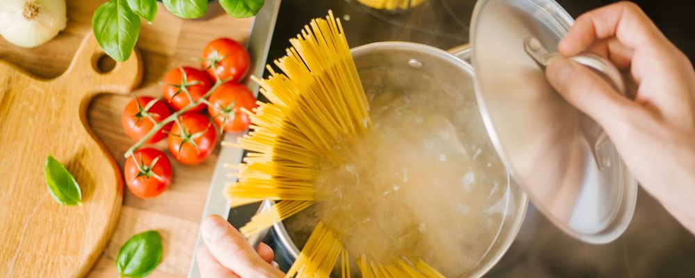Process of cooking homemade italian pasta. Lifestyle background. Man droping spaghetti into boiling water. Closeup. Horizontal.