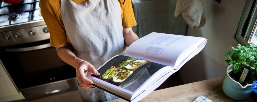 Happy woman reading a cookbook in the kitchen