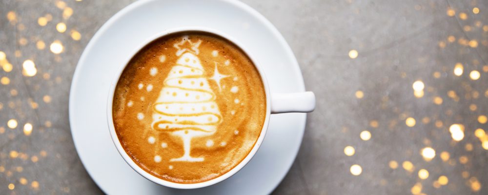 Tasty cappuccino with Christmas tree latte art with some blurred lights. Holiday concept.