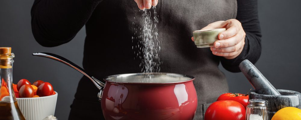 The chef preparations spaghetti and pasta, salt water, against a dark background, the concept of cooking. Woman salting water before cooking pasta fusilli.