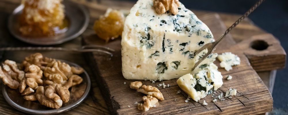Danish blue cheese on a wooden board with walnut kernels. dark background