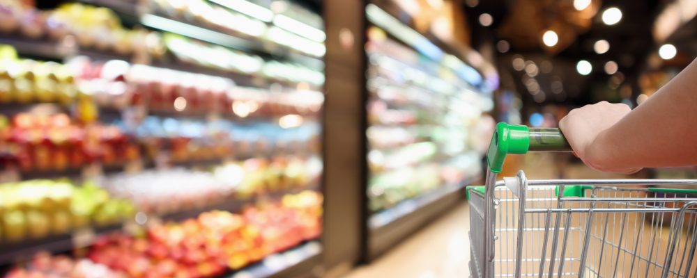woman hand hold supermarket shopping cart with abstract blur organic fresh fruits and vegetable on shelves in grocery store defocused bokeh light background