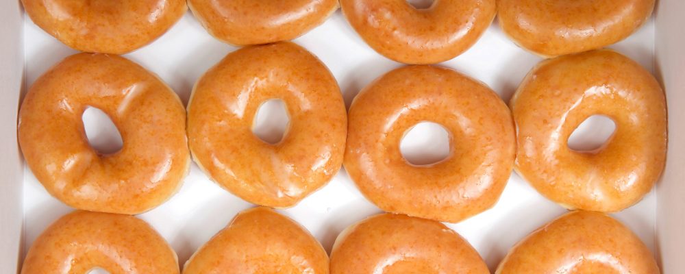 Top view flat lay of plain glazed donuts in a white box isolated. One dozen donuts. The original glazed donut has remained peoples favorite throughout history.