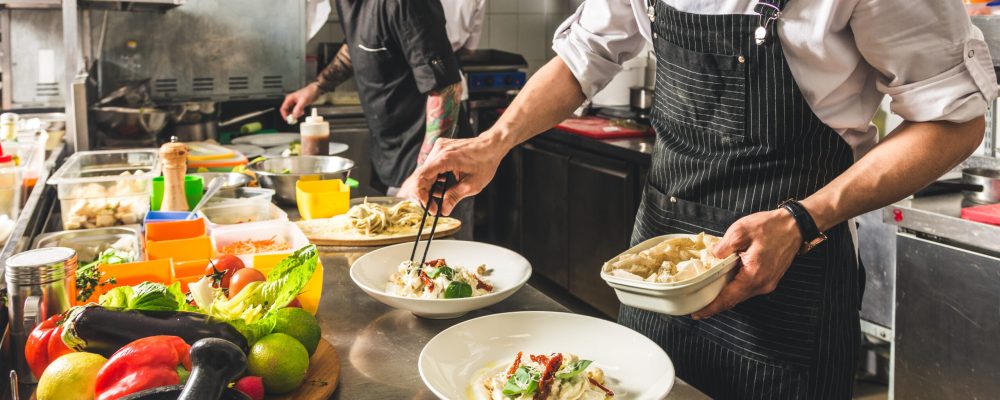 Professional chef cooking in the kitchen restaurant at the hotel, preparing dinner. A cook in an apron makes a salad of vegetables and pizza