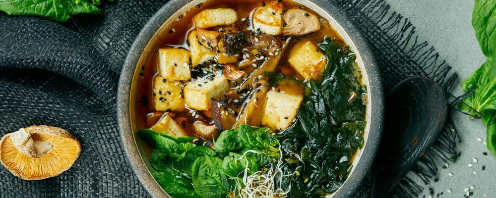 Fresh vegetarian miso soup with shiitake mushrooms, tofu cheese and seaweed on a gray cloth. Healthy, balanced food. Top view. Copy space