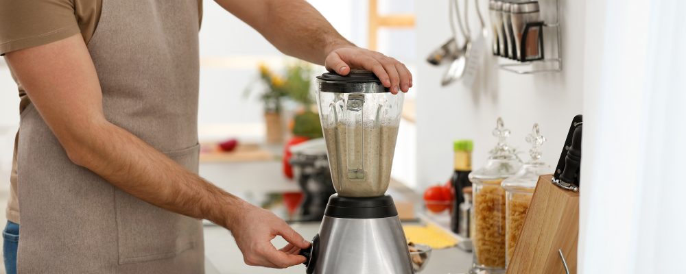 Young man using blender to cook cream soup in kitchen, closeup