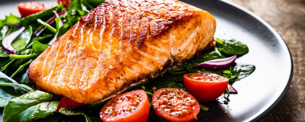 Fried salmon steak with vegetables on wooden table
