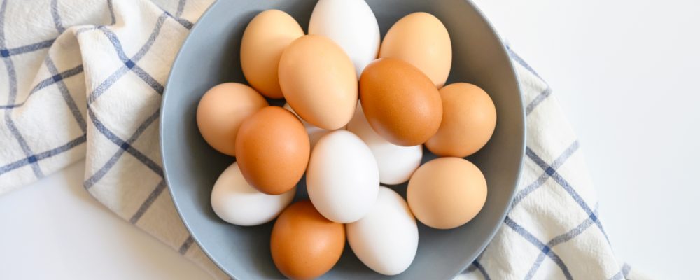 chicken eggs white and brown color in a gray plate on a checked kitchen towel on a white table. concept farm products and natural nutrition
