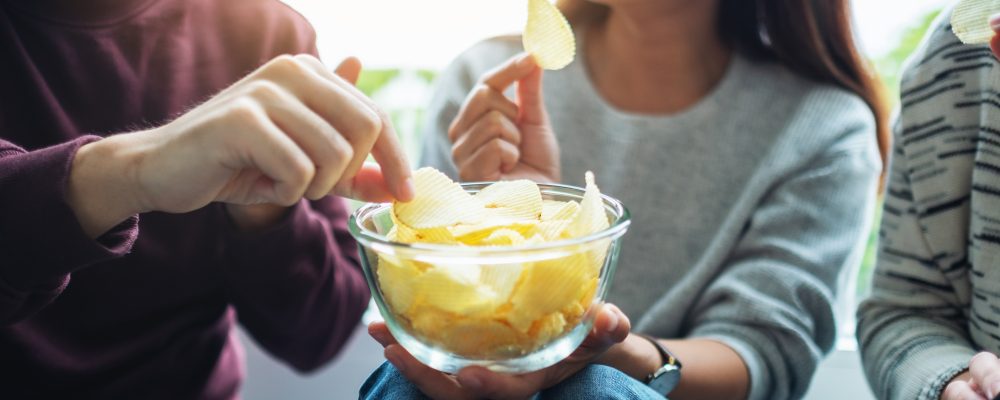 Closeup image of friends sharing and eating potato chips at home party together
