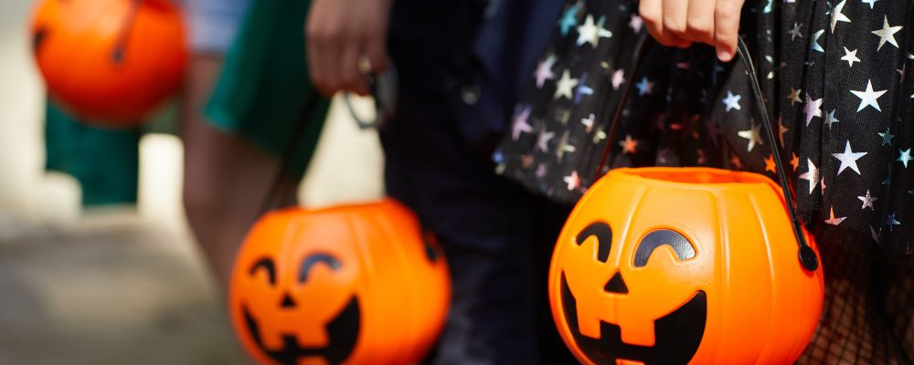 Close-up of children with pumpkins bags playing trick or treat outdoors