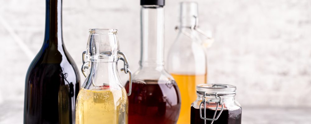 Original glass bottles with different vinegar on a marble table against a background of a white brick wall. Copy space. Horizontal.