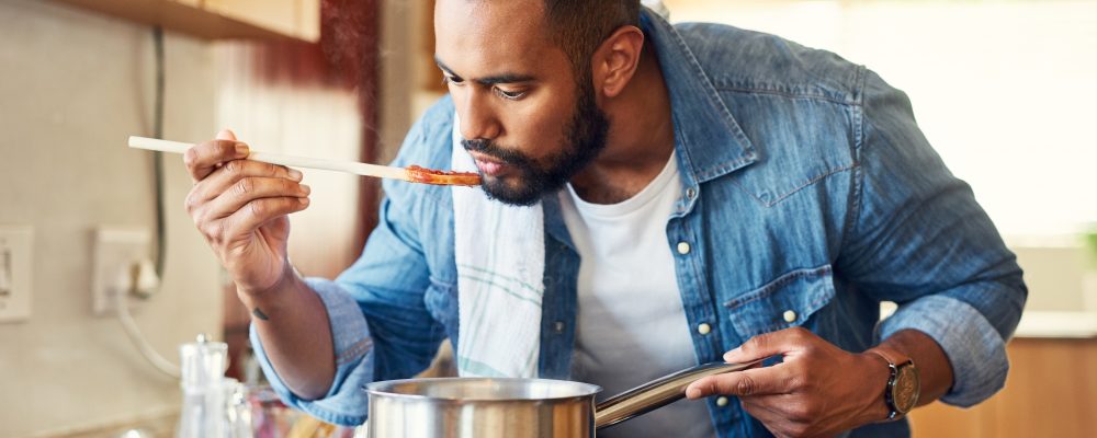 Shot of a man using a wooden spoon to taste his food while cooking.