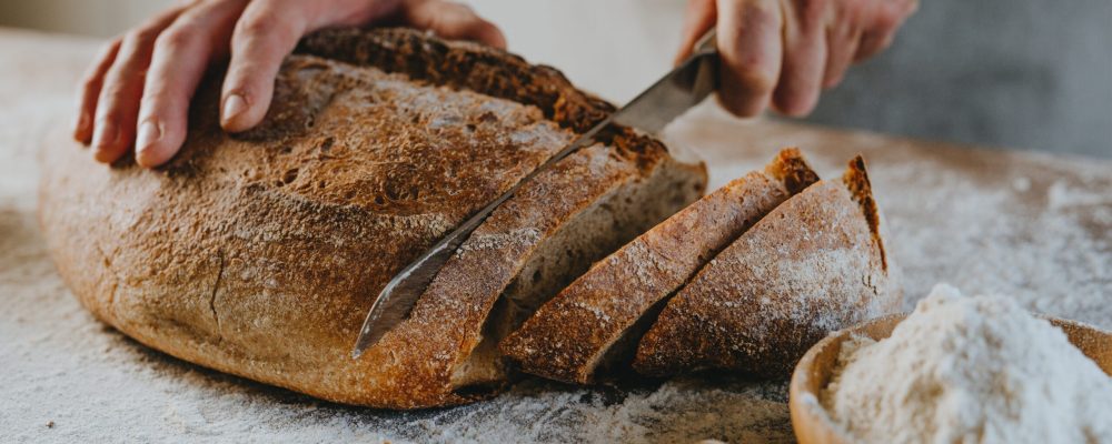Unrecognizable young man in apron cutting homemade whole grain bread. Selective focus.