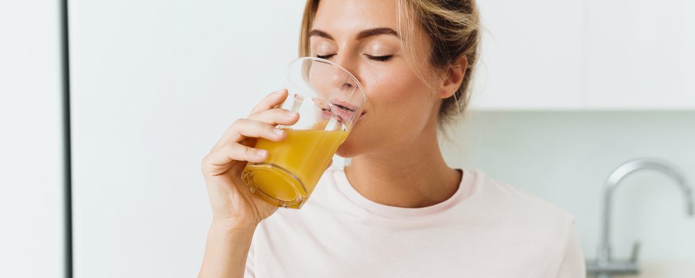 Young woman drinking freshly squeezed homemade orange juice in white kitchen