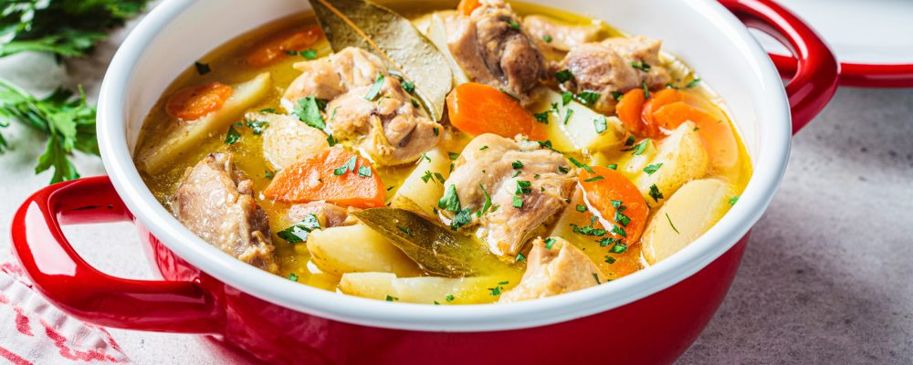 Chicken stew with potatoes and carrots in red pot. Chicken soup with vegetables and herbs. Comfort food recipe.