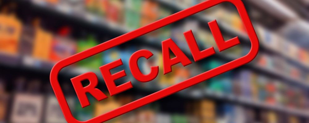 Blurry interior of a grocery store aisle behind large red Recall text