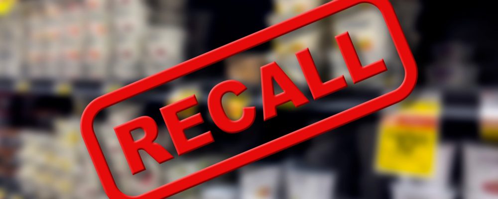 Blurry interior of a grocery store aisle behind large red Recall text