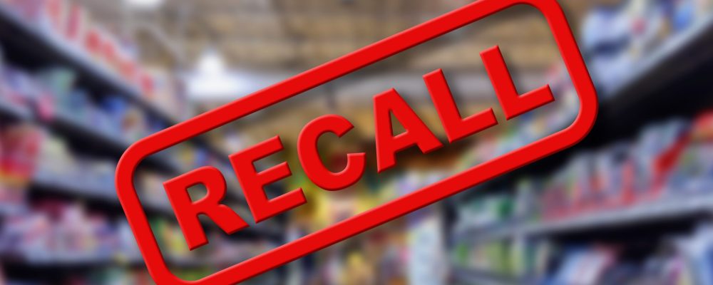 Blurry interior of a grocery store aisle behind large red Recall text