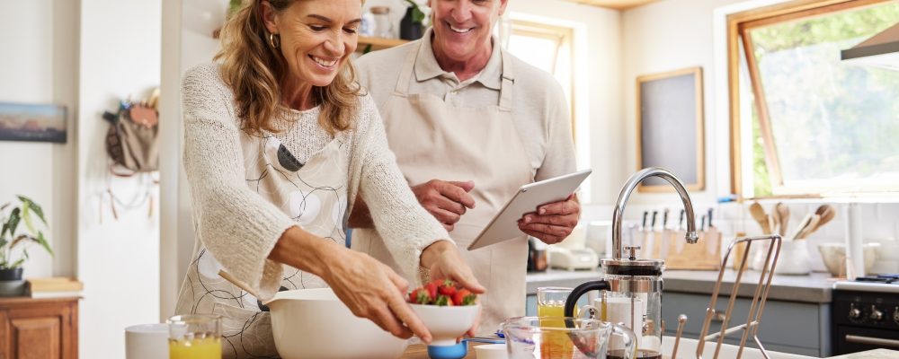 Tablet, cooking and internet with a senior couple baking using a recipe in the kitchen of their retirement home. Food, technology and love with an elderly man and woman pensioner preparing a meal.
