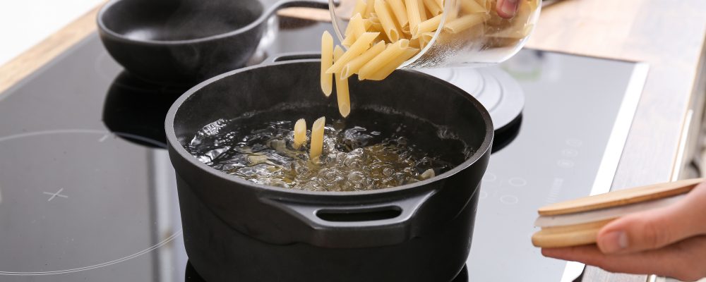Woman pouring raw pasta into pot with boiling water on stove