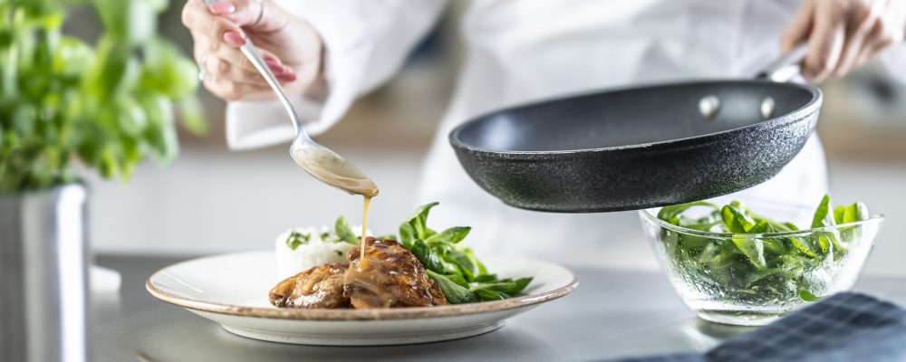 Female cook finishing food with sauce on counter in restaurant or hotel kitchen. The chef prepares the food just before taking it to the restaurant.