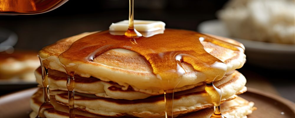 A stack of pancakes with syrup being poured on top