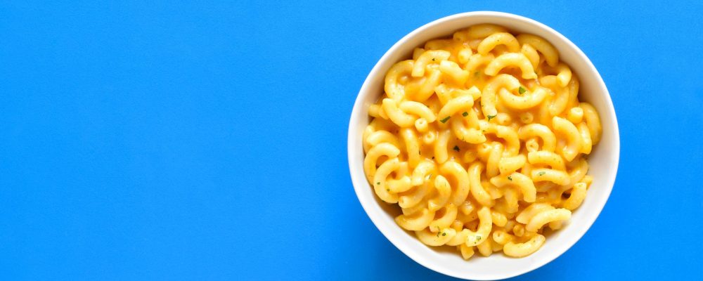 Macaroni and cheese in bowl over blue background with copy space. Top view, flat lay