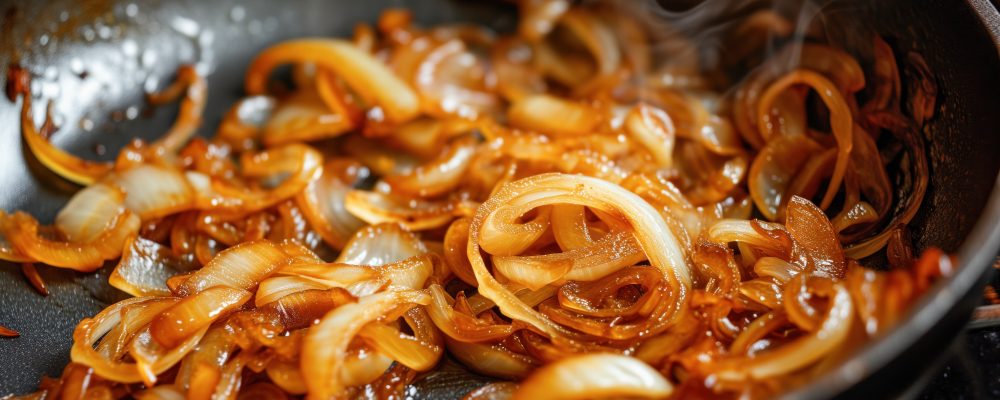 Golden caramelized onions cooking in a skillet, releasing aromatic steam.