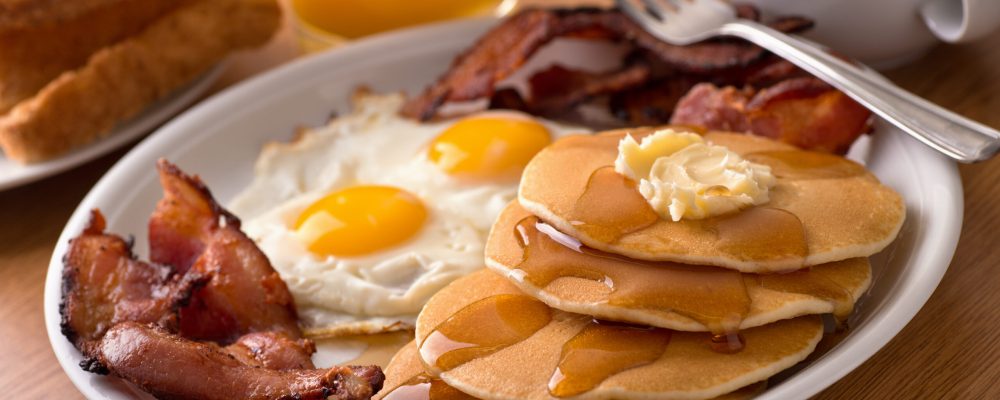 A delicous home style breakfast with crispy bacon, eggs, pancakes, toast, coffee, and orange juice.