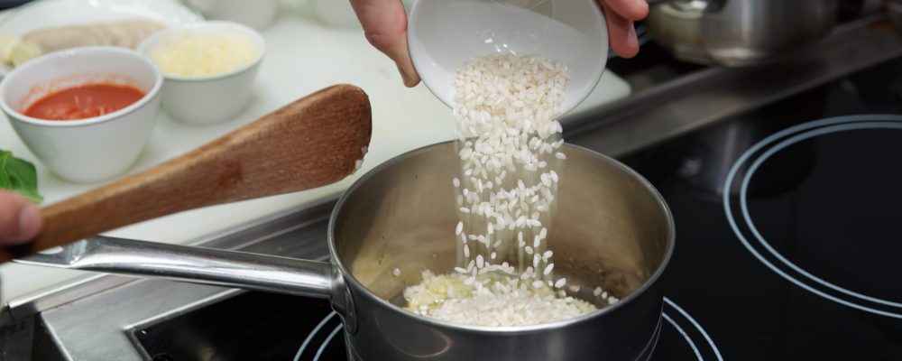 Chef is pouring rice in stewpan to cook risotto