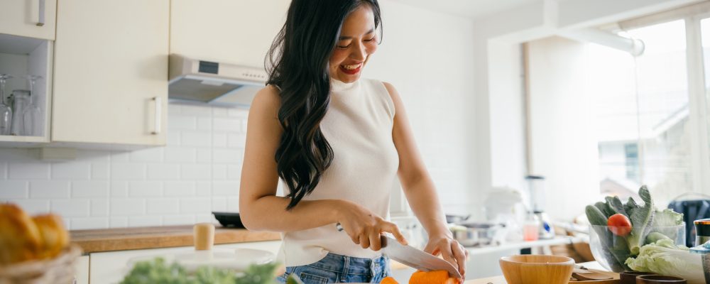 A young woman happily chopping vegetables in a bright, modern kitchen with natural light streaming through the windows.
